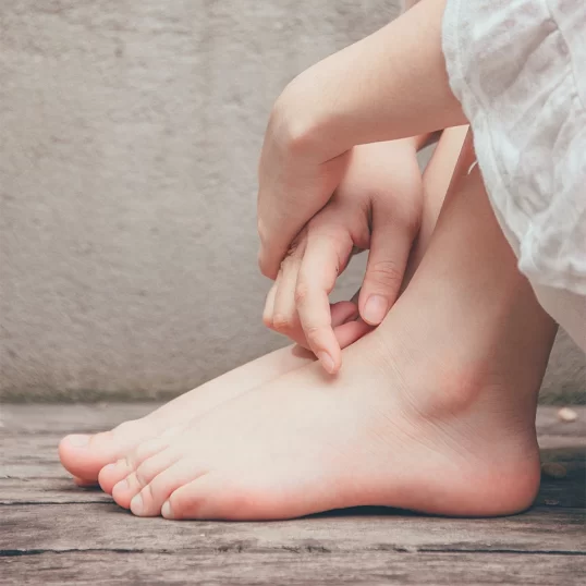 A person seated on a rustic wood floor, close up of their hands folded over their bare feet.